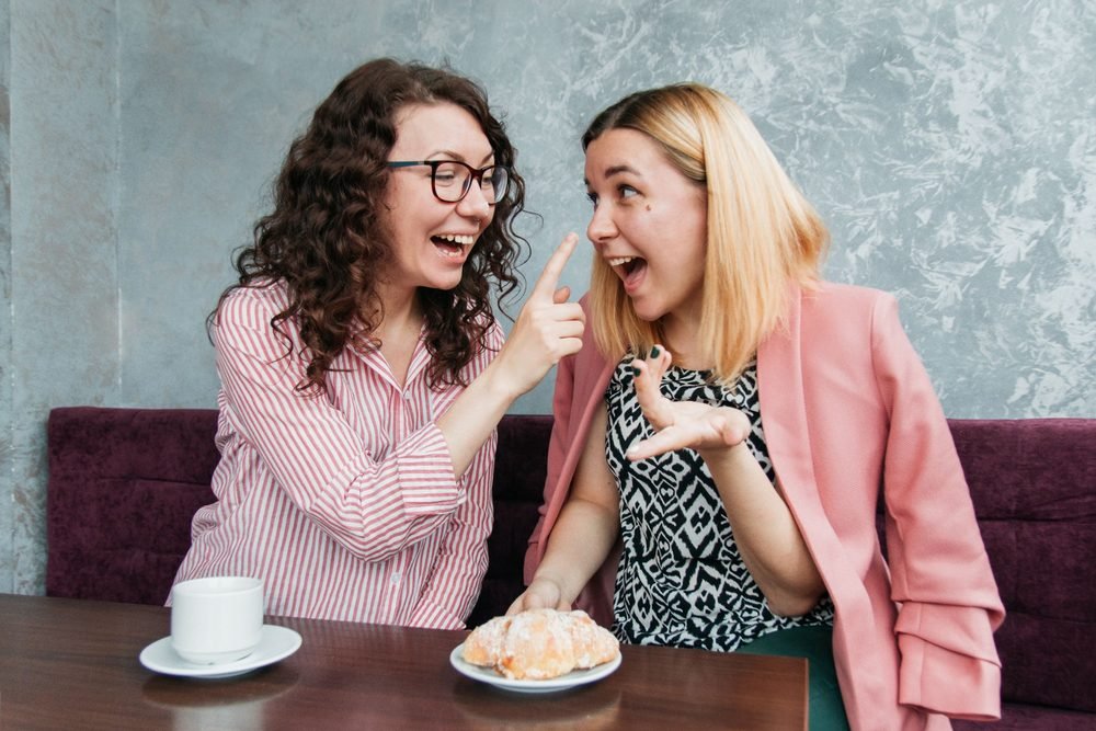 Two friends laughing together at a café table